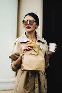 Young woman holding food and drink against wall