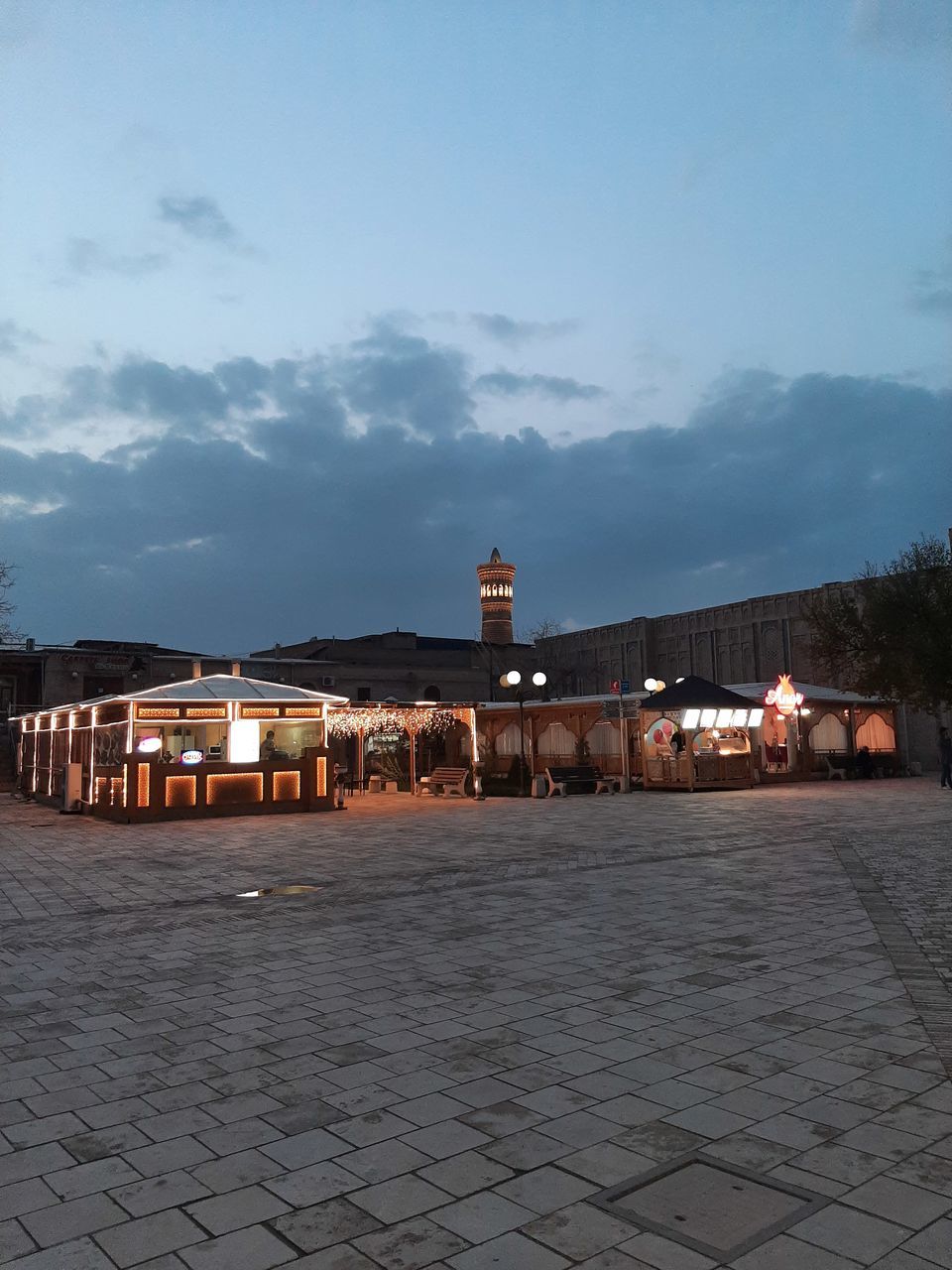 ILLUMINATED STREET AMIDST BUILDINGS AGAINST SKY AT DUSK