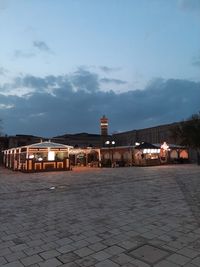 Illuminated street by buildings against sky at dusk