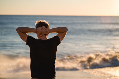 Rear view of man standing at beach sky during sunset