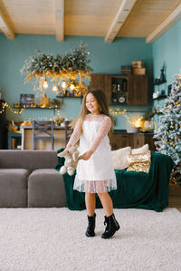 A beautiful smiling seven-year-old girl dances with a stuffed toy in the living room decorated 