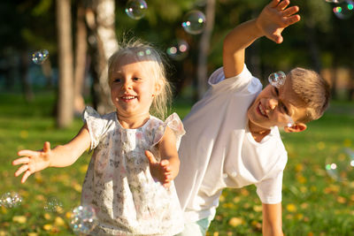 Brother and sister playing with bubbles against trees