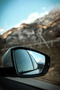 Close-up of sunglasses on side-view mirror against sky