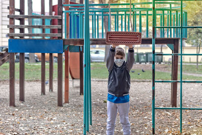 Little boy playing with a swing and wearing face mask in the park due to covid-19 pandemic.