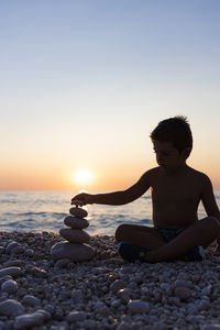 Little child playing with stones on the beach at sunset