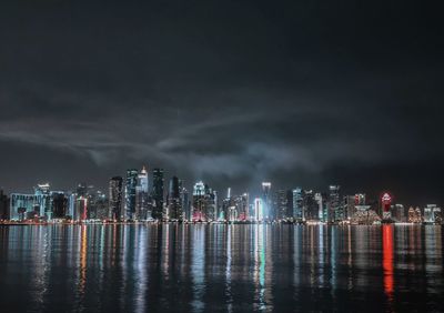 Illuminated buildings by river against sky at night