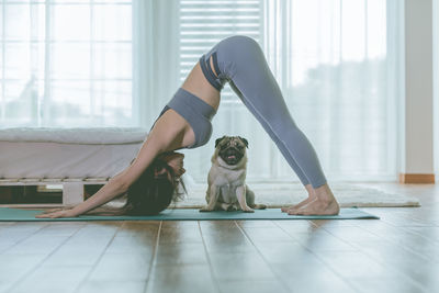 Full length side view of woman exercising at home with dog