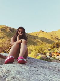 Portrait of woman sitting on mountain against clear sky