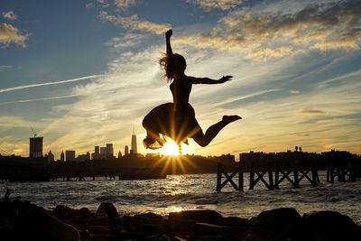Silhouette man jumping in sea against sky during sunset