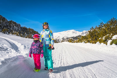 Mother and daughter standing on a snowy road with forest and mountains in background, andorra