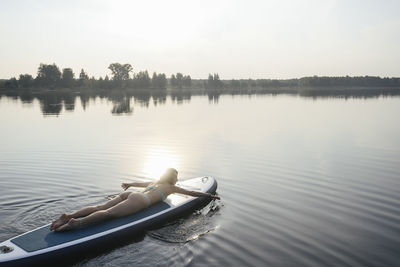 Woman paddling with hand lying on paddleboard at sunset