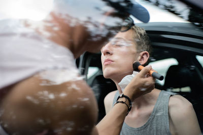 Artist applying make-up on man seen through car window