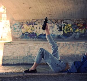 Low section of woman with leg up lying by canal in tunnel