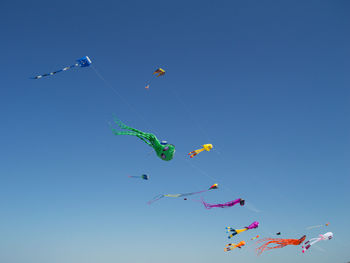 Low angle view of kites flying against clear blue sky