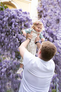 Father play,have fun outdoor with baby girl,daughter on background of purple,very peri wistaria tree