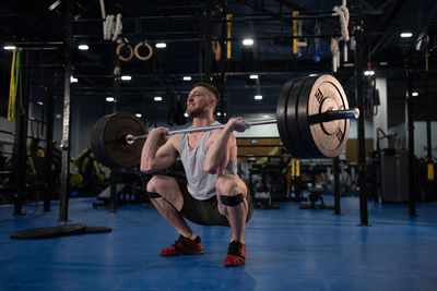 Weightlifter squatting with barbell in gym