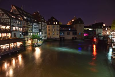 Illuminated buildings by river against sky at night