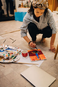 Female artist painting on paper while crouching at art studio