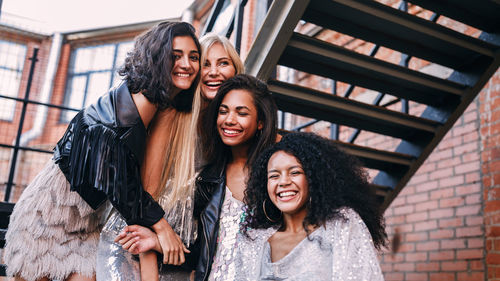 Low angle view of cheerful young female friends standing on staircase against building