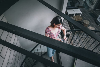High angle view of woman using smart phone while standing on staircase