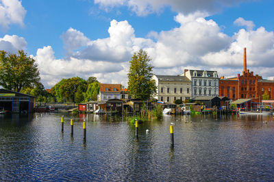 Canal in front of houses in town against cloudy sky