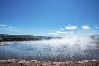Smoke emitting from strokkur geyser amidst landscape against blue sky