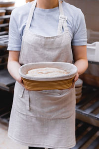 Hands of a baker holding dough in a wooden mold, against the backdrop of a bakery and workplace