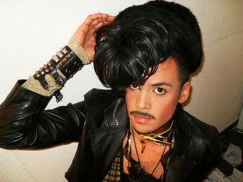 Portrait of young man wearing wig and make-up against wall