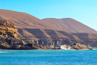 Scenic view of sea and mountains against clear blue sky