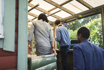 Rear view of male friends entering log cabin during summer party