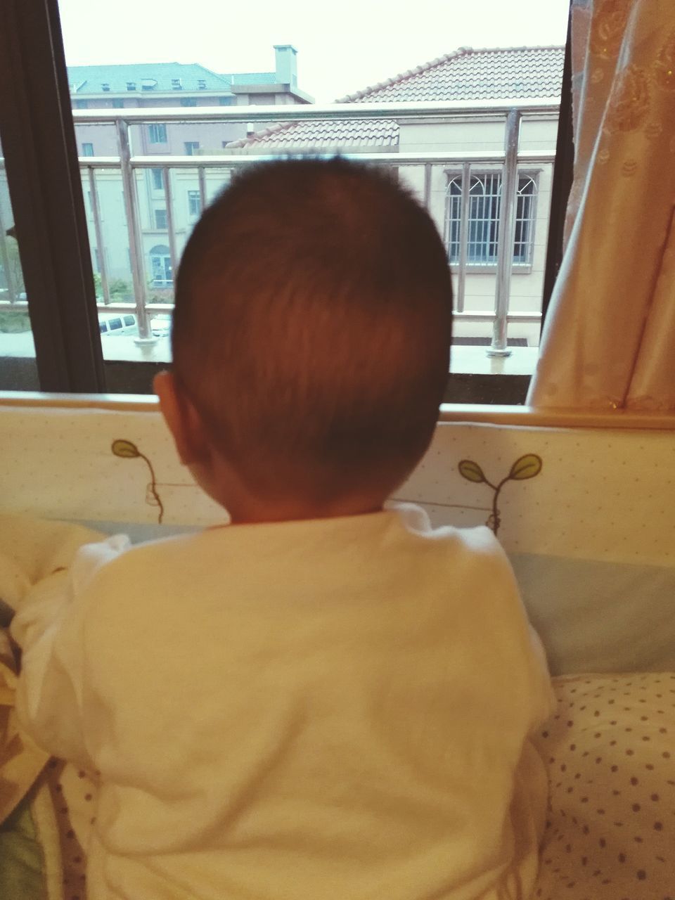 REAR VIEW OF BOY SITTING ON BED IN BEDROOM