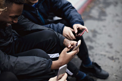 Social media addicted male friends sitting on street in city during winter