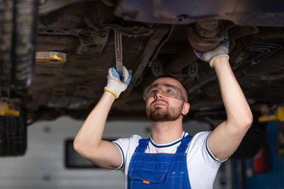 A young man auto mechanic in overalls at his workplace repairs the car's suspension