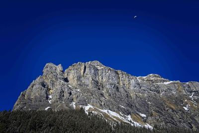 Low angle view of rocky mountain against clear blue sky