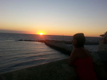 Woman looking at sea against sky during sunset