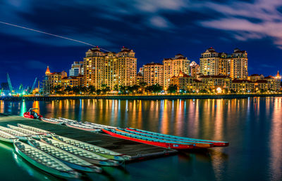 Illuminated city by river against sky at night