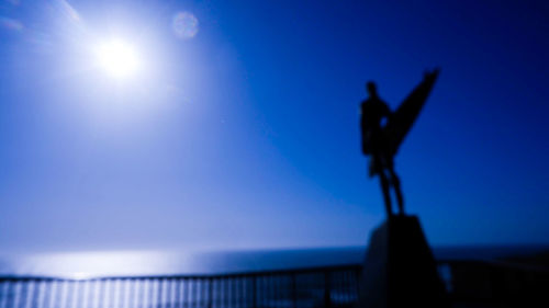 Low angle view of silhouette statue against blue sky on sunny day