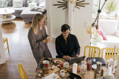 High angle view of happy couple having breakfast while working at home