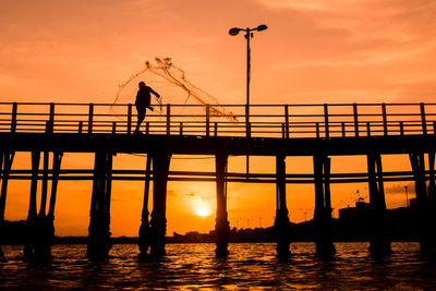 Silhouette people standing on bridge against sky during sunset