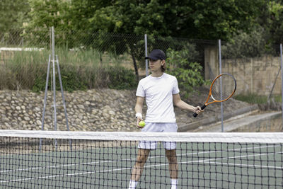 Shot from across the court of a young tennis player returning the ball to his opponent