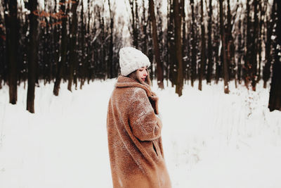 Photo of young beautiful woman in fur coat standing on the white snow in winter forest. girl is happ