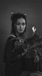 Portrait of young woman holding mask against gray background