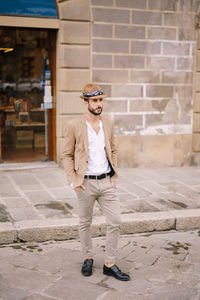 Groom wearing hat standing against wall