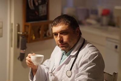 Thoughtful mature doctor with coffee sitting in hospital