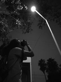 Low angle view of man photographing palm tree against sky