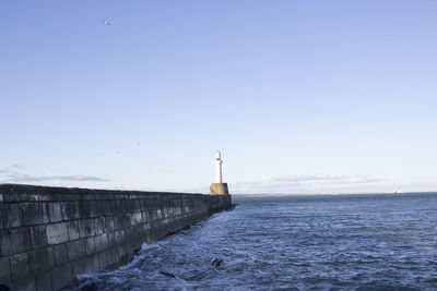 Lighthouse by sea against clear sky