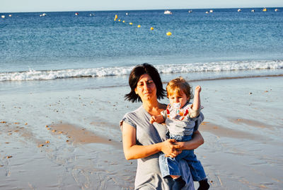 Mother carrying son while standing at beach