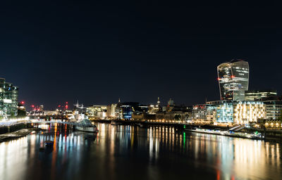 Illuminated buildings by river against clear sky at night