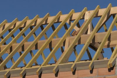 Low angle view of roof beams against clear sky during sunny day at construction site