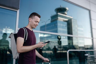 Traveler ordering taxi via mobile app. smiling man with backpack looking at phone at airport. 